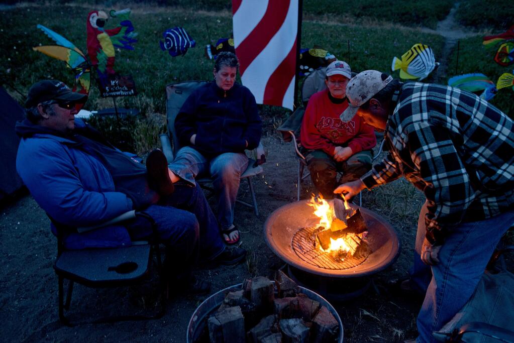 Bill Austin of North Highlands, California, right, places a new log on the fire as his wife P.J., second from right, and their friends Craig and Melanie Baillie of Lincoln, California look on, at Doran Beach Campgrounds in Bodega Bay, Calif., on May 22, 2014. (Alvin Jornada / For The Press Democrat)