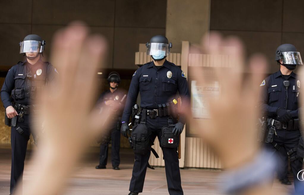 A demonstrator raises her hands as police officers stand guard in front of the City Hall during a protest Monday, June 1, 2020, in Anaheim, Calif., over the death of George Floyd on May 25 in Minneapolis. (AP Photo/Ringo H.W. Chiu)