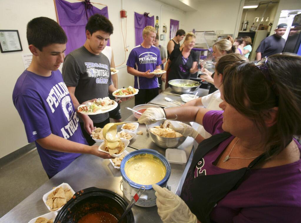 Petaluma High football players have their lunch prepared and served by moms like Michelle Goddard, mom of Casey, serving up cheese for nachos during football camp on Tuesday August 12, 2014.