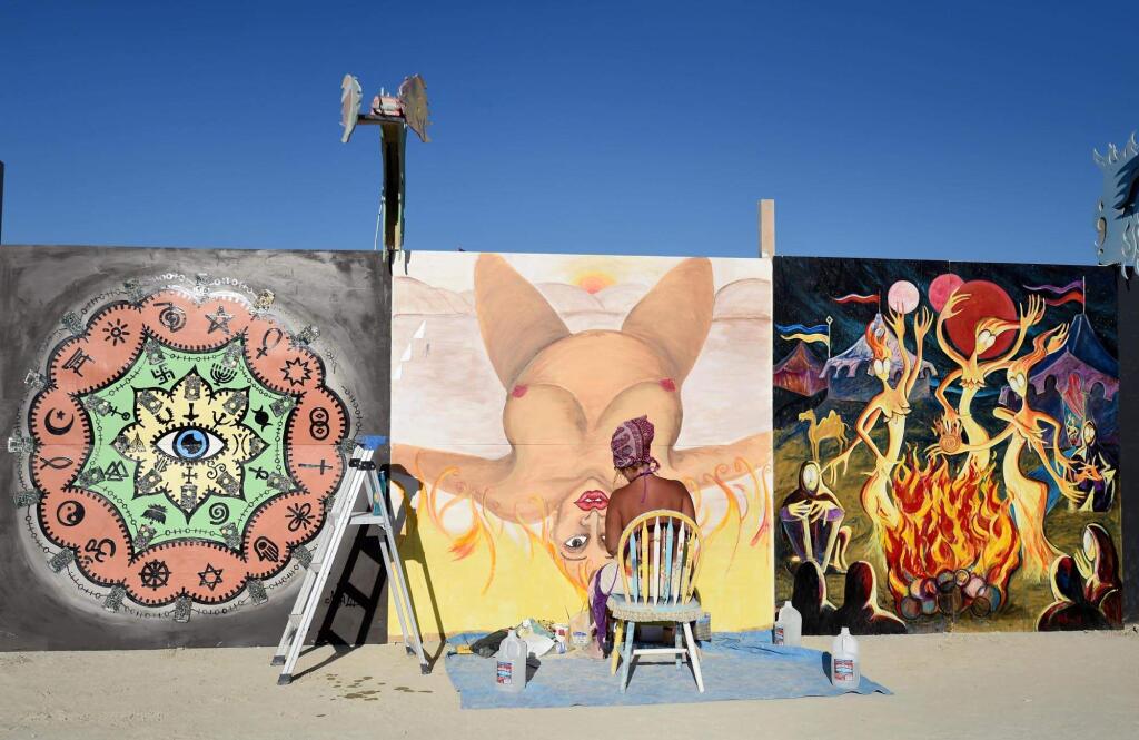 Artist Christina Minor paints on one of the panels around center camp at Burning Man in the Black Rock Desert in Gerlach, Nev. on Aug. 24, 2014. The event was temporarily closed on Monday, when it was supposed to open, due to heavy rains. (AP Photo/Reno Gazette-Journal, Andy Barron)