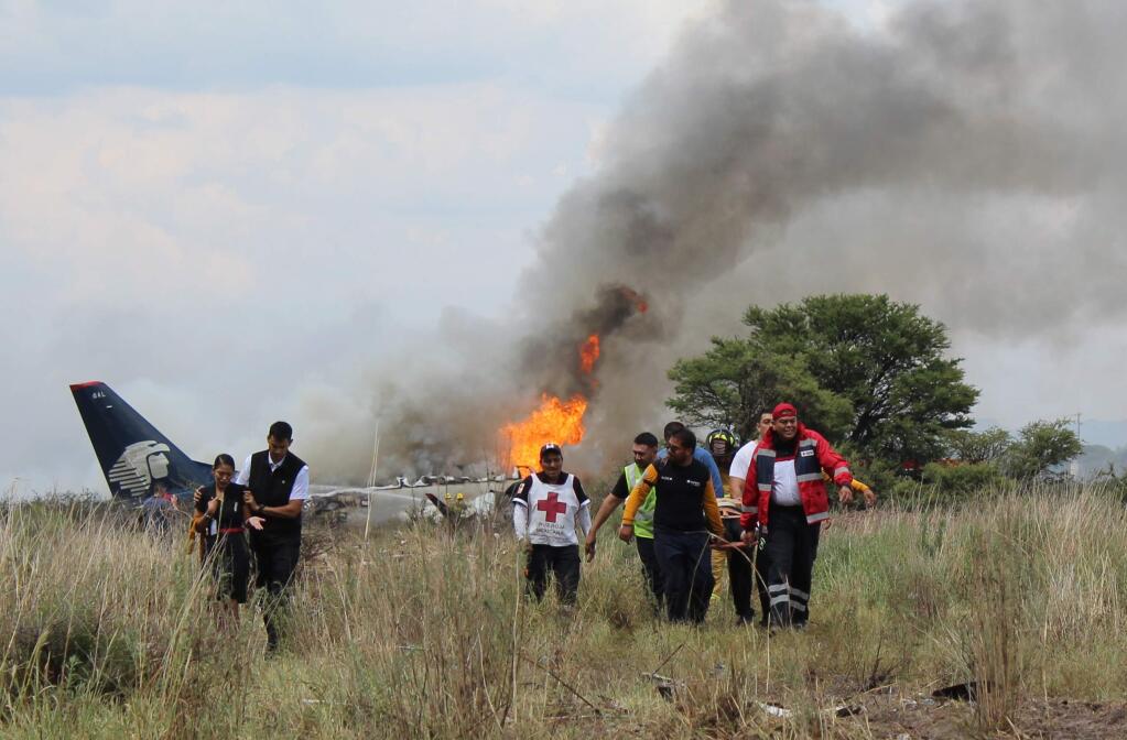 In this photo released by Red Cross Durango communications office, Red Cross workers and rescue workers carry an injured person on a stretcher, right, as airline workers, left, walk away from the site where an Aeromexico airliner crashed in a field near the airport in Durango, Mexico, Tuesday, July 31, 2018. The jetliner crashed while taking off during a severe storm, smacking down in a field nearly intact then catching fire, and officials said it appeared everyone on board escaped the flames. (Red Cross Durango via AP)