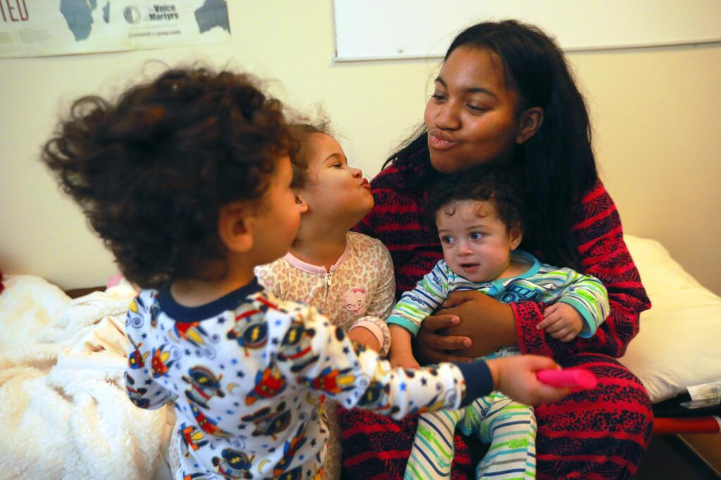 From right, Cymone Weddington, right, gives goodnight kisses to her children Zachariah, 5 months, Jazzmariah, 4, and Noahmiah, 22 months before bedtime at a pop-up shelter at the Calvary Chapel of Santa Rosa on Wednesday night. Weddington and her family evacuated from the Extended Stay Hotel on Mendocino Ave. (photo by John Burgess/The Press Democrat)