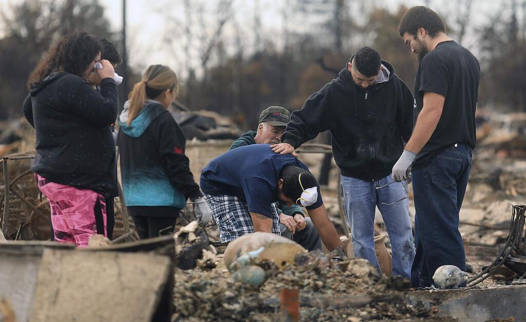 Ben Hernandez, middle, finds their family pet in the ashes of their Hopper Lane home, comforted by his son, Ben Jr. with Herenadez's wife Renee, in pink, and the rest of his family in Coffey Park, Friday Oct. 20, 2017 in Santa Rosa, Calif. Northern California residents who fled a wildfire in the dead of night with only minutes to spare returned to their neighborhoods Friday for the first time in nearly two weeks to see if anything was standing. (Kent Porter/The Press Democrat via AP)