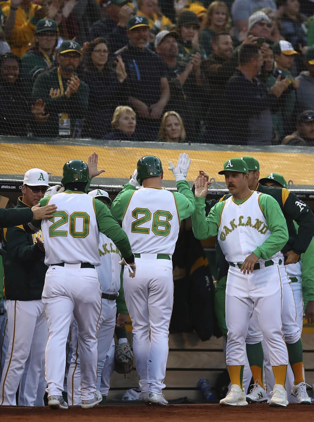 The Oakland Athletics' Mark Canha (20) and Matt Chapman (26) are congratulated by manager Bob Melvin, left, and Daniel Mengden, right, after scoring against the Chicago White Sox during the first inning Tuesday, April 17, 2018, in Oakland. (AP Photo/Ben Margot)