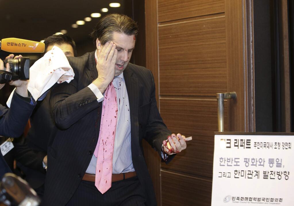 U.S. Ambassador to South Korea Mark Lippert placing his right hand on his face leaves a lecture hall for a hospital in Seoul, South Korea, Thursday, March 5, 2015 after being attacked by a man. Lippert was in stable condition after the man screaming demands for a unified North and South Korea slashed him on the face and wrist with a knife, South Korean police and U.S. officials said. The board at right reads: 'U.S. Ambassador to South Korea Mark Lippert's lecture.' (AP Photo/Yonhap, Kim Ju-sung) KOREA OUT