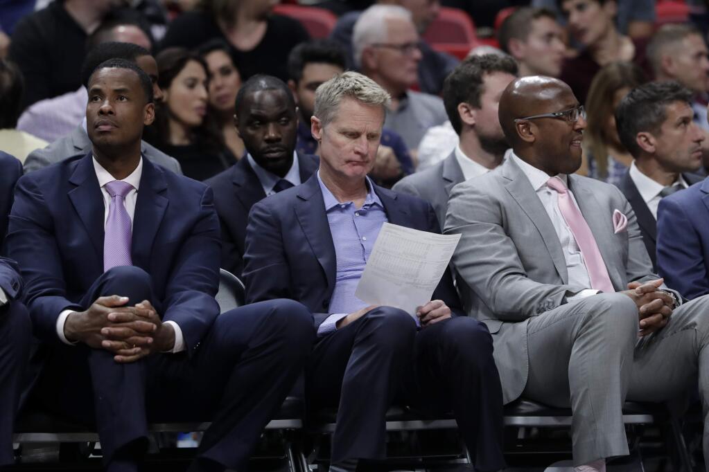 Golden State Warriors head coach Steve Kerr, center, sits with assistant coaches Jarron Collins, left, and Mike Brown, right, during the second half against the Miami Heat, Friday, Nov. 29, 2019, in Miami. The Heat won 122-105. (AP Photo/Lynne Sladky)
