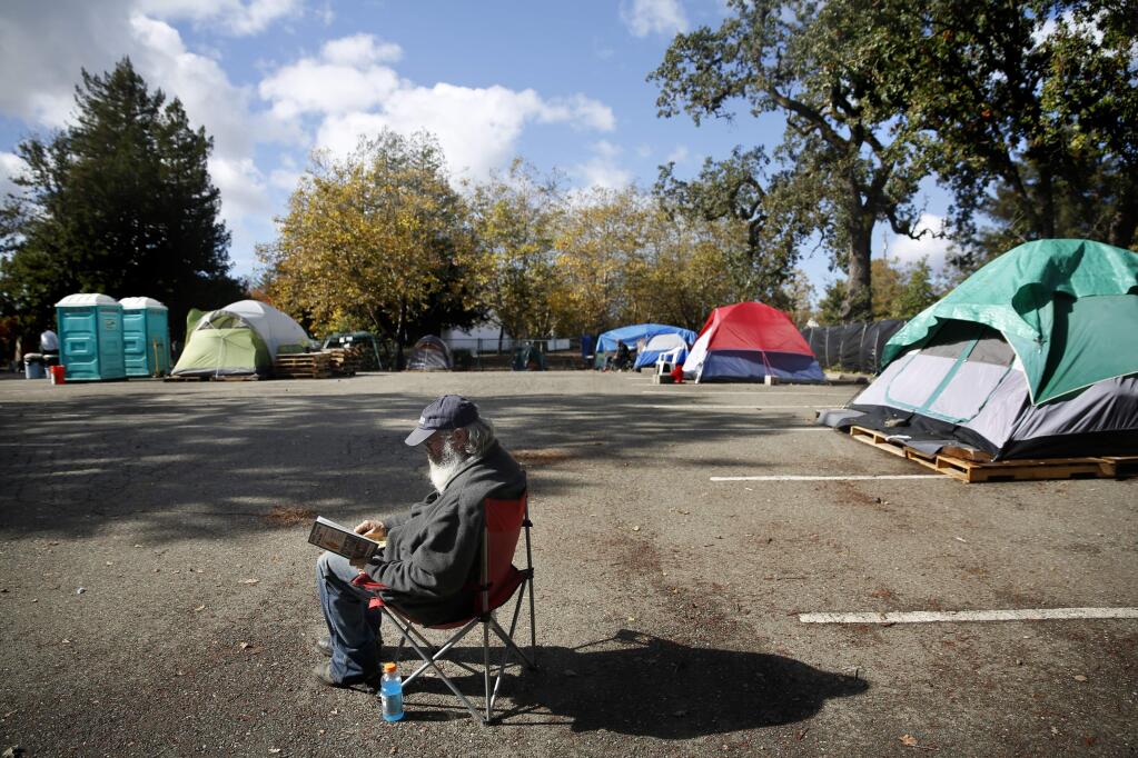 Russ Samson sits in the sun and reads outside his tent at the homeless encampment at the former Sonoma County Water Agency campus in Santa Rosa, on Monday, Nov. 2, 2015. (BETH SCHLANKER / The Press Democrat)