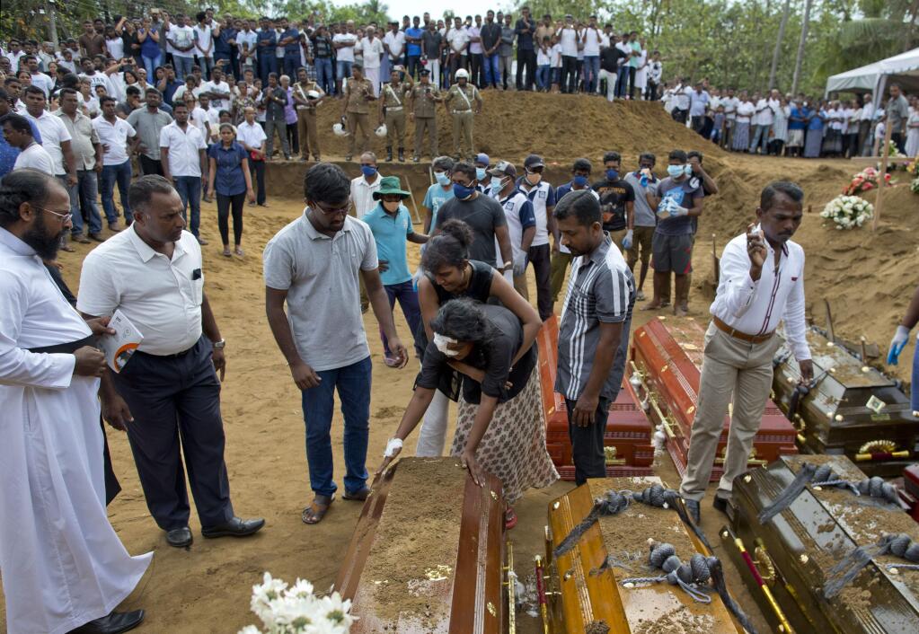 Anusha Kumari, center, holds a coffin during a mass burial for her husband, two children and three siblings, all victims of Easter Sunday's bomb blast in Negombo, Sri Lanka, Wednesday, April 24, 2019. Kumari, 43, was left childless and a widow when suicide bombers launched a coordinated attack on churches and luxury hotels in and just outside Sri Lanka's capital, Colombo. (AP Photo/Gemunu Amarasinghe)