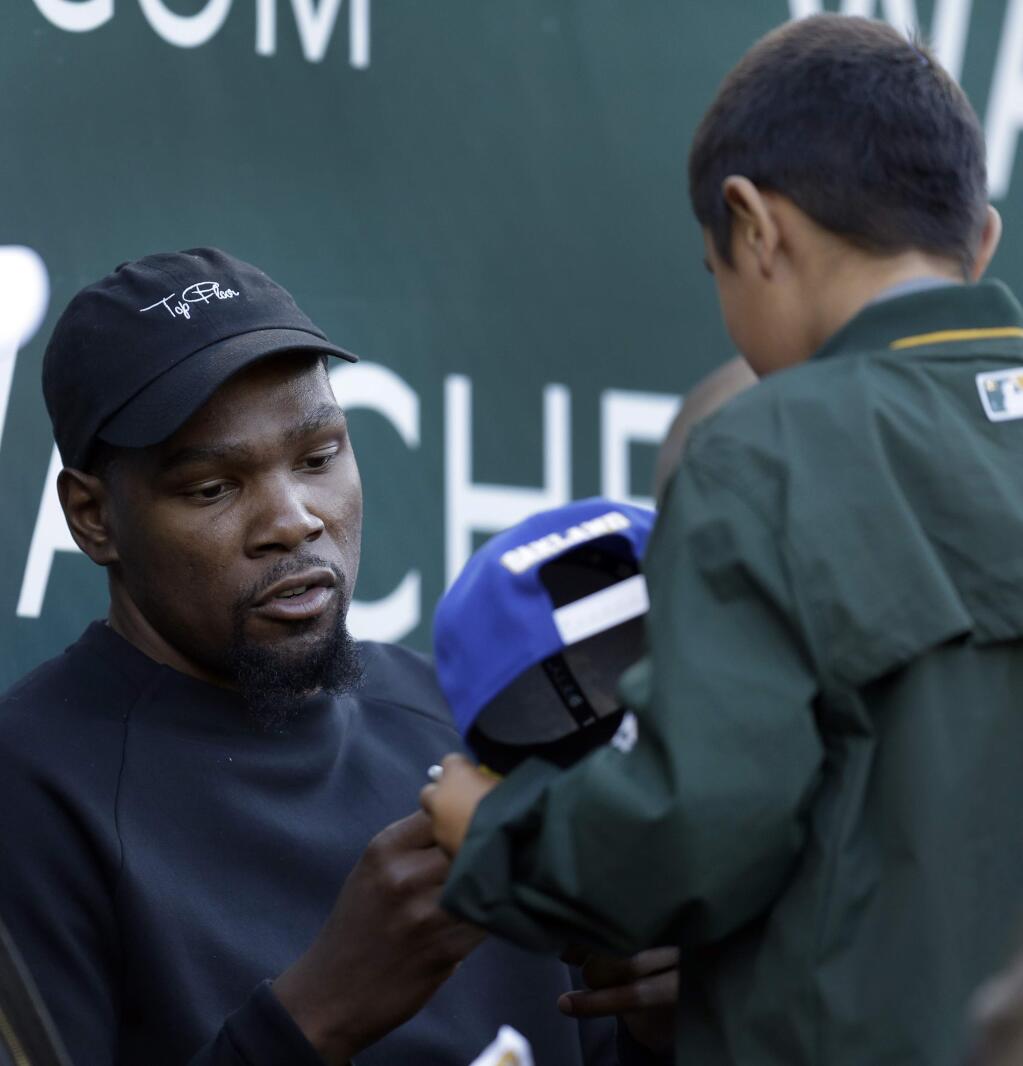 Golden State Warriors' Kevin Durant signs an autograph during the first inning of a baseball game between the Los Angeles Angels and Oakland Athletics, Tuesday, May 9, 2017, in Oakland, Calif. (AP Photo/Ben Margot)