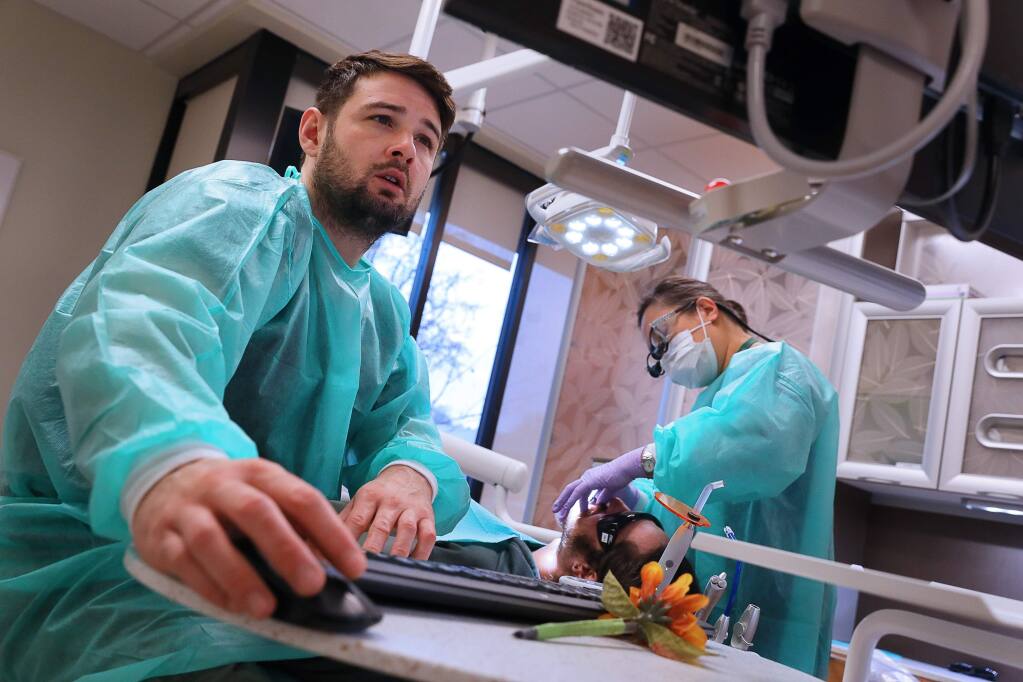 Registered dental assistant William Guzman, left, enters patient information while Dr. Cynthia Hom examines Alex Garakian in the dental center of the Santa Rosa Community Health-Dutton Campus, in Santa Rosa on Friday, February 8, 2019. (Christopher Chung/ The Press Democrat)