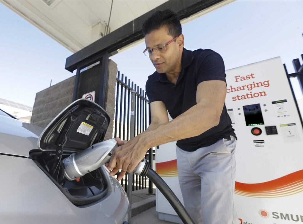 FILE - In this Sept. 17, 2015, file photo, Darshan Brahmbhatt, plugs a charger into his electric vehicle at the Sacramento Municipal Utility District charging station in Sacramento, Calif. (AP Photo/Rich Pedroncelli, File)