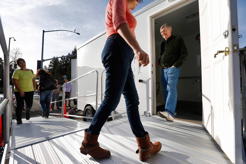 Roseanna Gonzalez, left, and Marge Lopez, center, and Lee Dibble, right, take turns looking inside the new portable bathroom-shower trailer, part of the Homeless Outreach Services Team (HOST) program run by Catholic Charities during the trailer's unveiling in front of city hall in Santa Rosa, California on Friday, February 12, 2016. (Alvin Jornada / The Press Democrat)