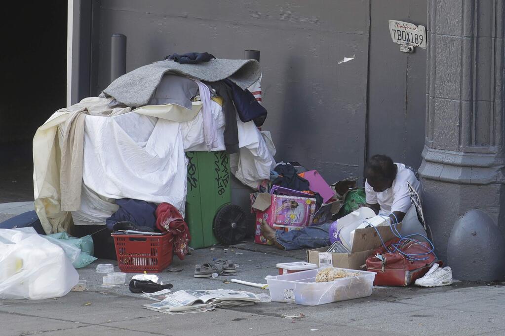 FILE - In this April 2, 2020, file photo, a homeless person sits on the street in San Francisco. San Francisco's mayor reported Friday, April 10, 2020, that 70 people at the city's largest homeless shelter have tested positive for COVID-19, infuriating advocates of the homeless who have been pushing the city for weeks to get people out of crowded shelters and into individual hotel rooms. (AP Photo/Jeff Chiu, File)