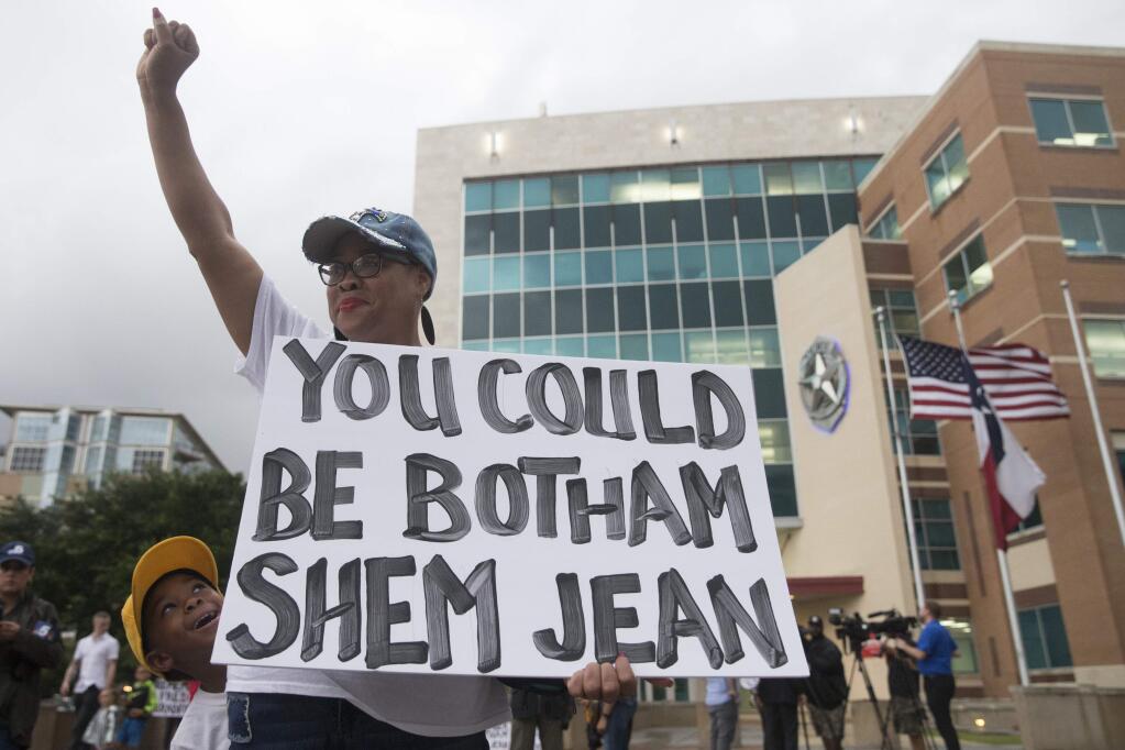 Dr. Pamela Grayson raises her fist as 'Young King' Solomon Grayson, 6, peaks behind her sign during a Mothers Against Police Brutality candlelight vigil for Botham Jean at the Jack Evans Police Headquarters on Friday, Sept. 7, 2018, in Dallas. Authorities are seeking a manslaughter warrant for the Dallas police officer who shot and killed Jean after she said she mistook his apartment for her own, police said Friday. (Shaban Athuman/The Dallas Morning News via AP)