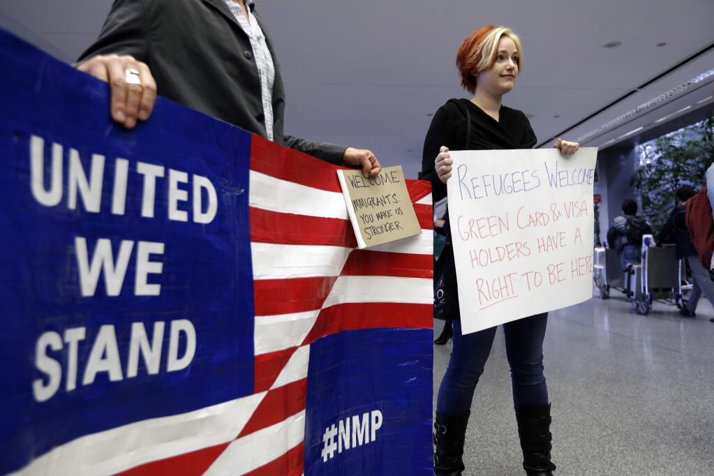 Robert May, left, and Sarah Dizio hold signs in the arrivals terminal at San Francisco International Airport to protest President Donald Trump's executive order that bars citizens of seven predominantly Muslim-majority countries from entering the U.S. Monday, Jan. 30, 2017, in San Francisco. (AP Photo/Marcio Jose Sanchez)