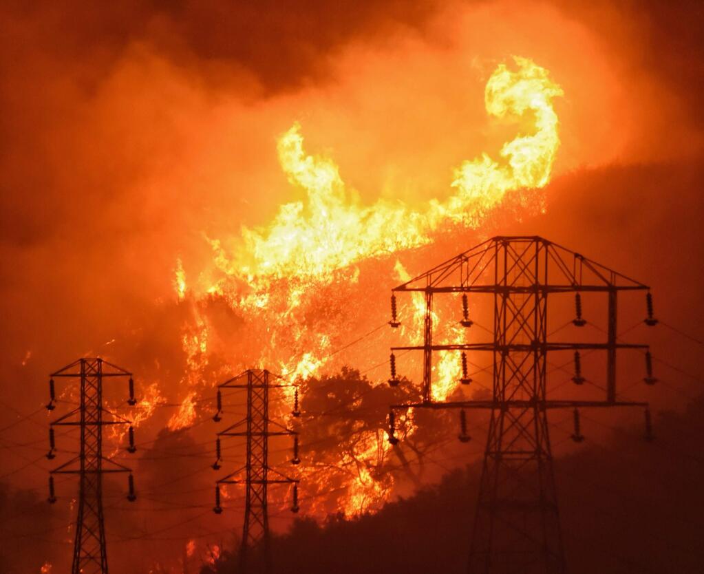 FILE - In this Dec. 16, 2017, file photo provided by the Santa Barbara County Fire Department, flames burn near power lines in Sycamore Canyon near West Mountain Drive in Montecito, Calif. California lawmakers raised concerns Thursday, Aug. 9, 2018, that a proposal from Gov. Jerry Brown to shield electrical utilities from some financial liability for wildfires would give them too much protection without ensuring the utilities safely maintain their equipment. (Mike Eliason/Santa Barbara County Fire Department via AP, File)