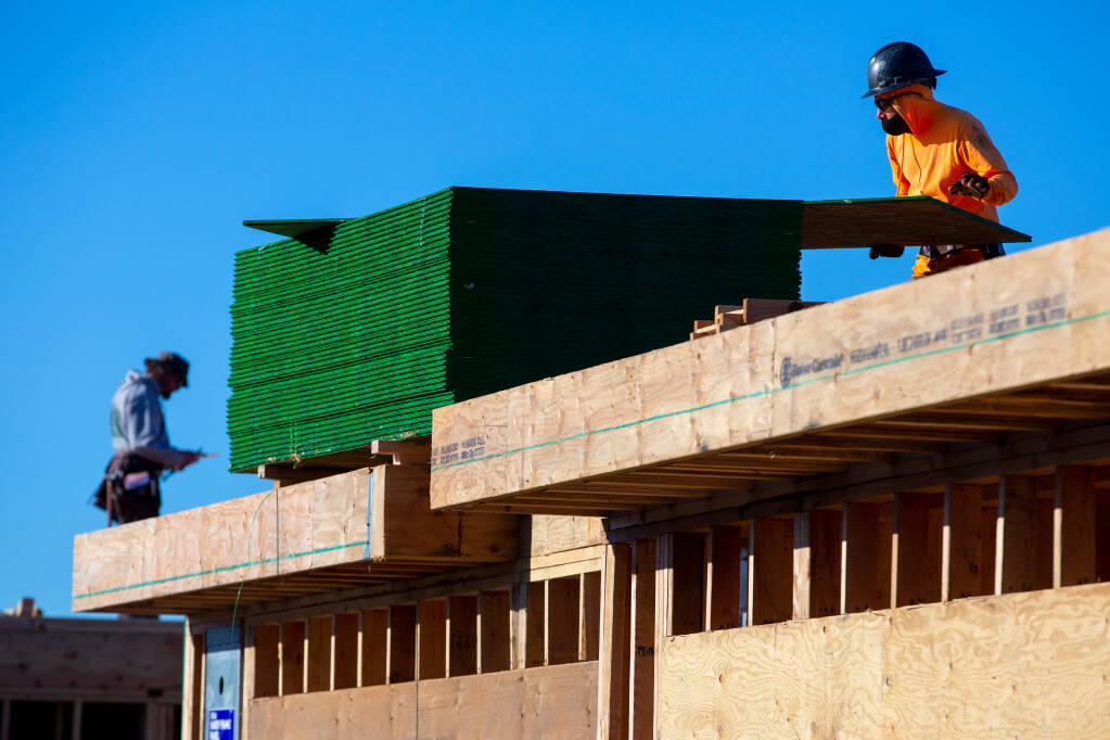 A construction worker pulls sheets of plywood to build up the second story of new townhouses in the Round Barn Village development in Santa Rosa on Dec. 22, 2020. (Alvin A.H. Jornada / The Press Democrat)