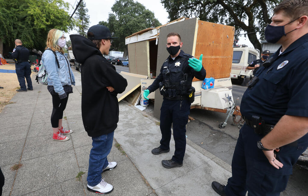 Santa Rosa Police Officer Tim Barrett explains to Michael Howard why his mother's trailer is being towed from Fremont Park, on Fifth Street, in Santa Rosa on Wednesday, July 29, 2020.  (Christopher Chung / The Press Democrat)