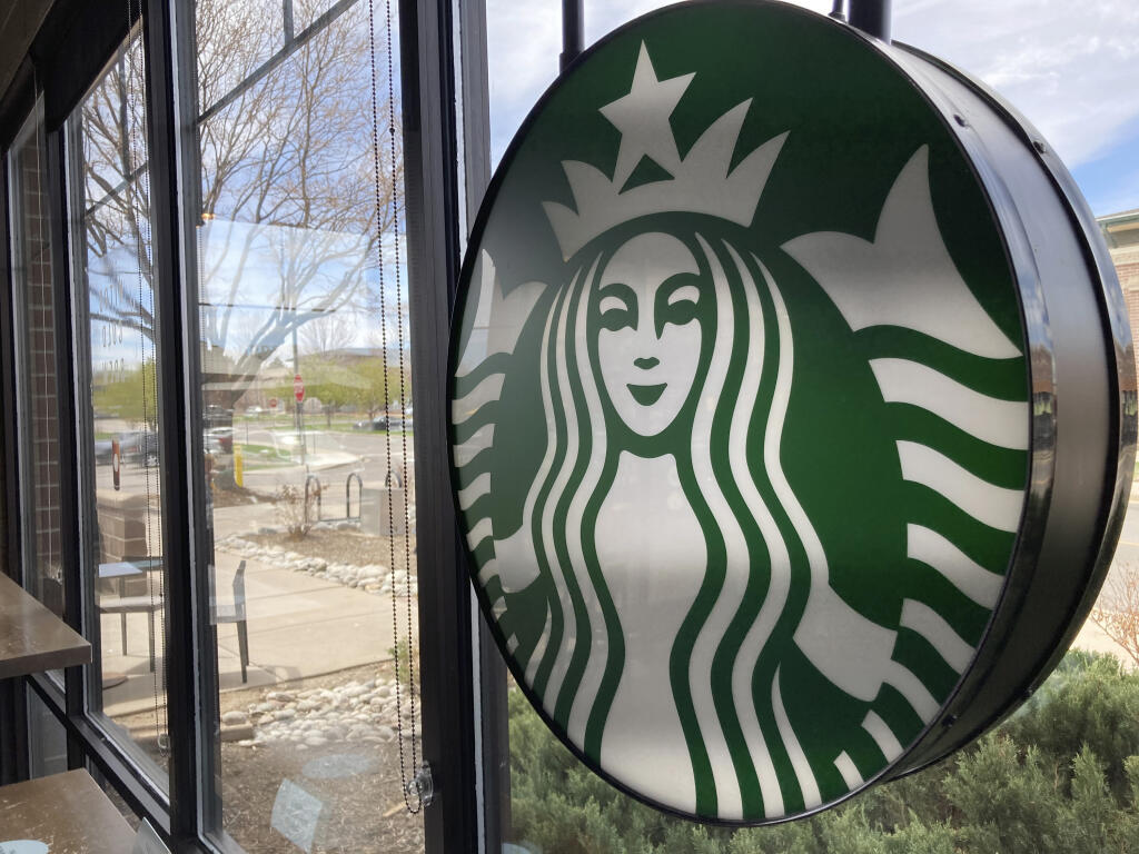 A sign bearing the corporate logo hangs in the window of a Starbucks open only to take-away customers in this photograph taken Monday, April 26, 2021, in southeast Denver. (AP Photo/David Zalubowski)