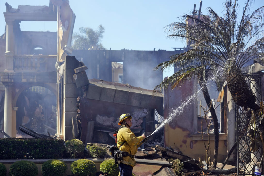 Firefighter Mike Mejia, of the National City Fire Dept, hoses down hot spots from a home in the aftermath of the Coastal Fire Thursday, May 12, 2022, in Laguna Niguel, Calif. (AP Photo/Marcio Jose Sanchez)