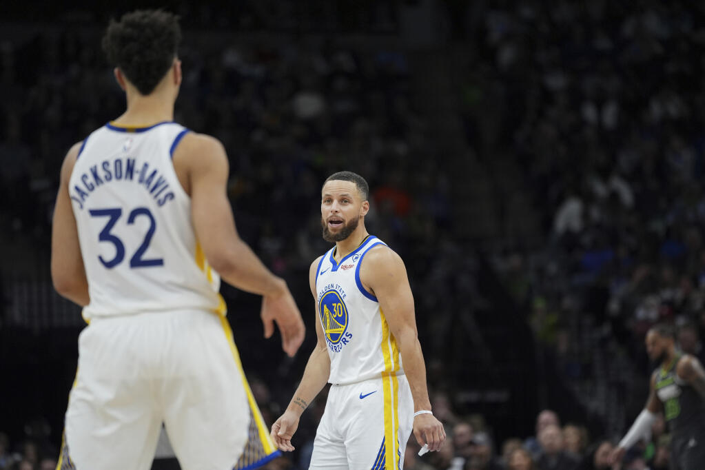 Warriors guard Stephen Curry looks toward forward Trayce Jackson-Davis during the second half of Sunday’s game against the Minnesota Timberwolves in Minneapolis. (Abbie Parr / ASSOCIATED PRESS)