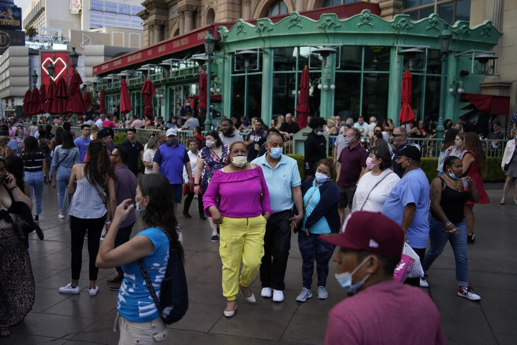 People walk along the Las Vegas Strip, Saturday, April 24, 2021, in Las Vegas. Las Vegas is bustling again after casino capacity limits were raised Saturday, May 1, to 80% and person-to-person distancing dropped to 3 feet (0.9 meters). (AP Photo/John Locher)