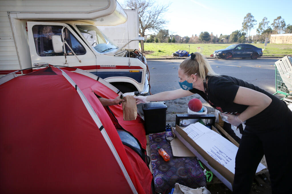 Jackie Nappi of Sonoma Applied Village Services (SAVS) hands Michael Arcadia a bag of snacks at the homeless encampment on Industrial Drive in Santa Rosa, California, on Monday, Jan. 18, 2021. (Beth Schlanker/ The Press Democrat)