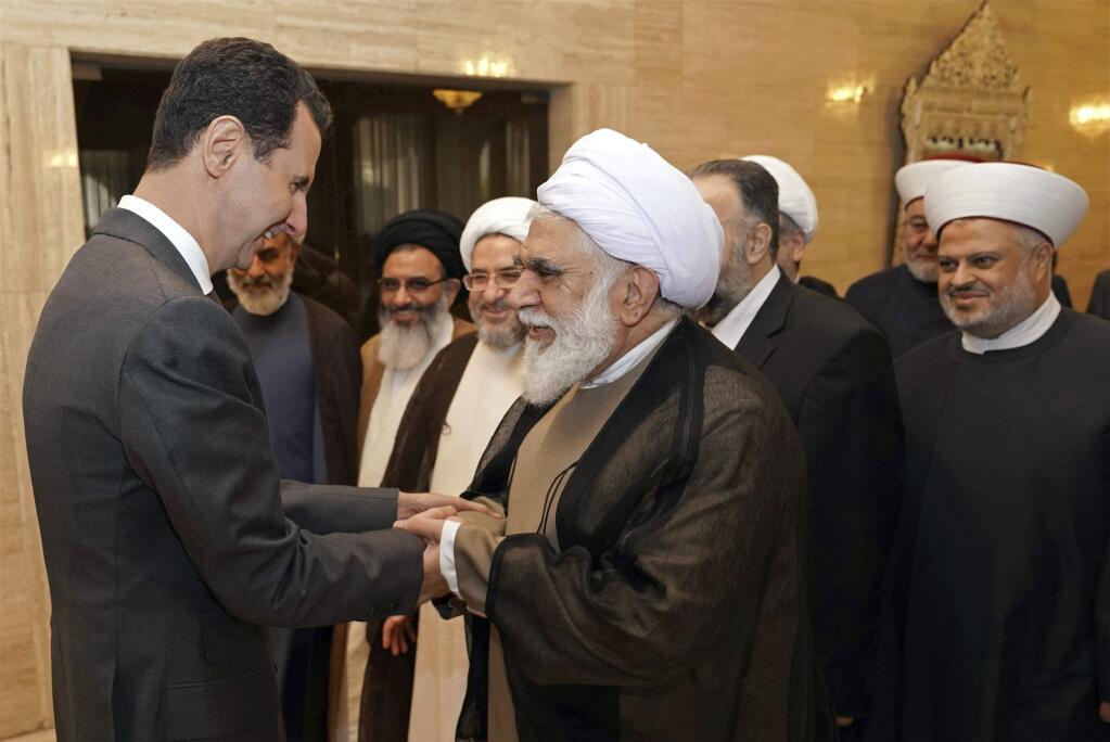 This photo released by the Syrian official news agency SANA, shows Syrian President Bashar Assad, left, meeting with a delegation of Muslim clerics from around the world, who took part in a two-day conference called, 'Unity of the Muslim World,' in Damascus, Syria, Wednesday, April 11, 2018. (SANA via AP)
