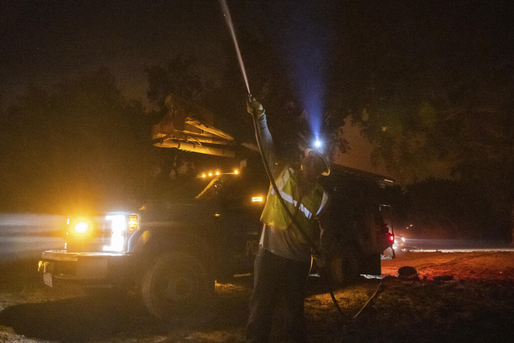 A Pacific Gas and Electric employee Sean Ohaire hoses down a telephone pole at the Zogg Fire near Igo, Calif., early Monday, Sep. 28, 2020. (AP Photo/Ethan Swope)