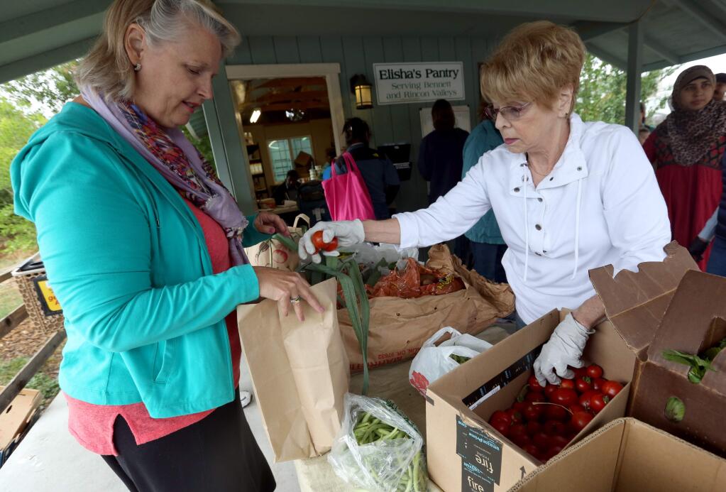 PHOTO: 2 BY CRISTA JEREMIASON/ THE PRESS DEMOCRAT -Pat Rosetti, right, fills a bag with fruits and vegetables for Terry Tamblin, who was picking up free food for two families at Elisha's Pantry.