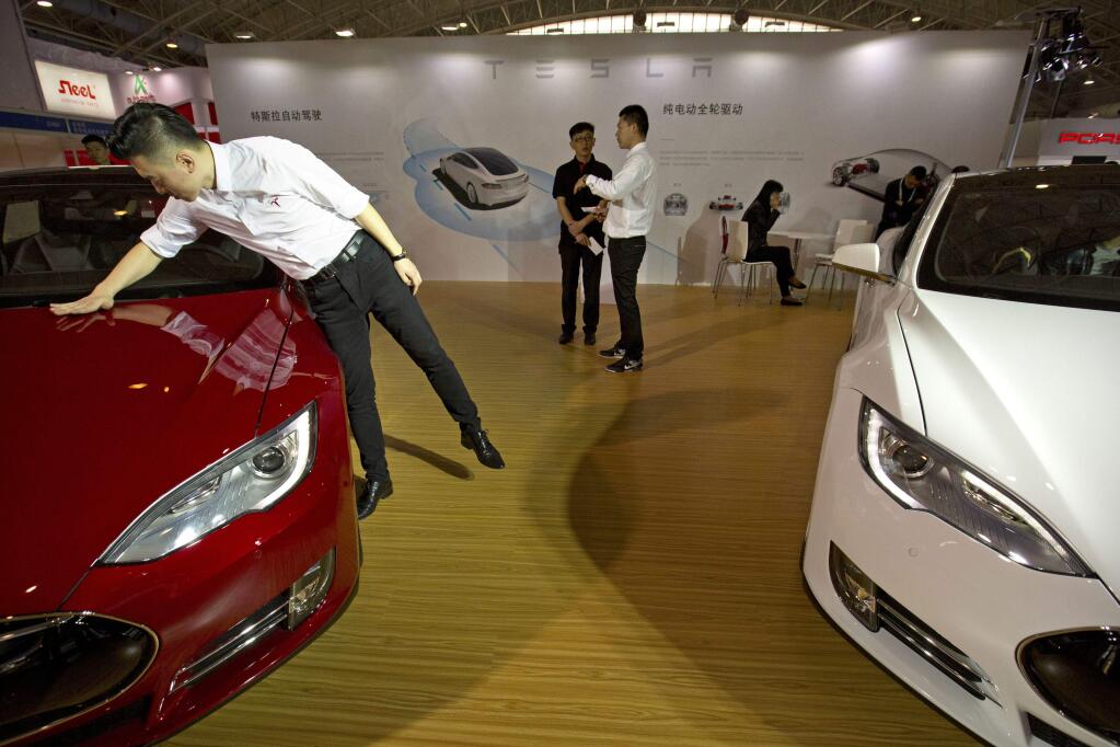 FILE - In this Monday, April 25, 2016, file photo, a staff member cleans the hood of a Tesla Model S electric car near a display advertising Tesla's self-driving features at the Beijing International Automotive Exhibition in Beijing, China. Tesla says it can't verify whether a vehicle autopilot system is to blame for the death of a Chinese man whose father claimed in a report broadcasted Wednesday, Sept. 14, 2016, on state television that the driver-assist feature was active at the time of his crash. (AP Photo/Mark Schiefelbein, File)