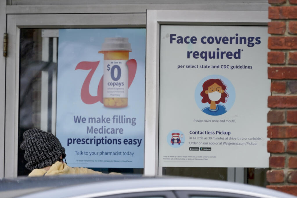 A patron opens the door with the signs requiring shoppers to comply with state COVID-19 guidelines to enter the Walgreens in Zelienople, Pa., Thursday, Jan. 28, 2021. (AP Photo/Keith Srakocic)