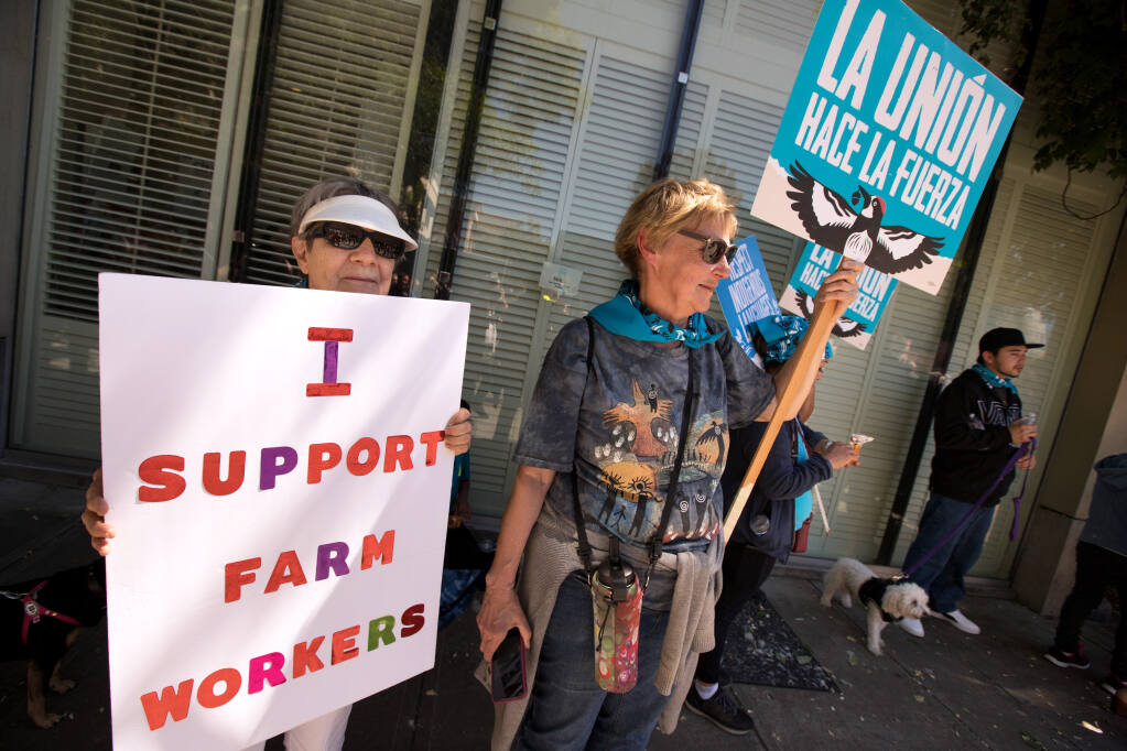 Valerie White, left, and Tessa Kraft, both of Healdsburg, right, holds signs to support protesters from North Bay Jobs with Justice as they demonstrate for farmworkers disaster pay near the Healdsburg Food & Wine Experience, Saturday, May 20, 2023, in Healdsburg. (Darryl Bush / For The Press Democrat)