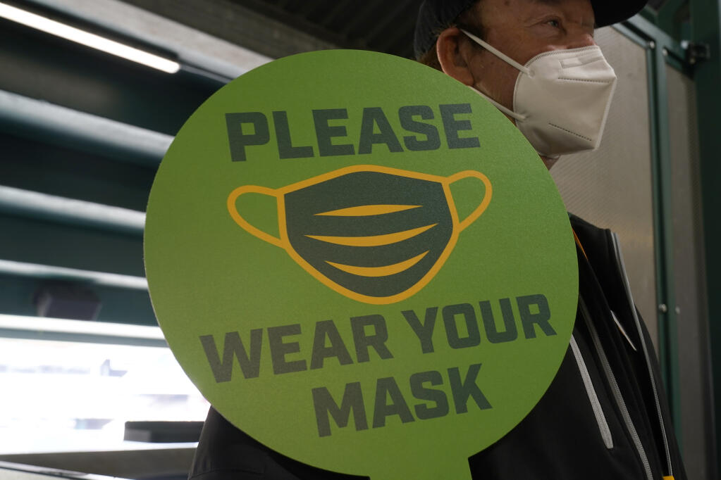FILE - In this April 3, 2021, file photo, a stadium worker holds up a sign for people to wear face masks before a baseball game between the Oakland Athletics and the Houston Astros in Oakland, Calif. California is keeping its rules for wearing facemasks in place until the state more broadly lifts its pandemic restrictions on June 15. State officials said Monday, May 17 that the delay will give people time to prepare, and for the state to make sure that virus cases stay low. (AP Photo/Jeff Chiu, File)