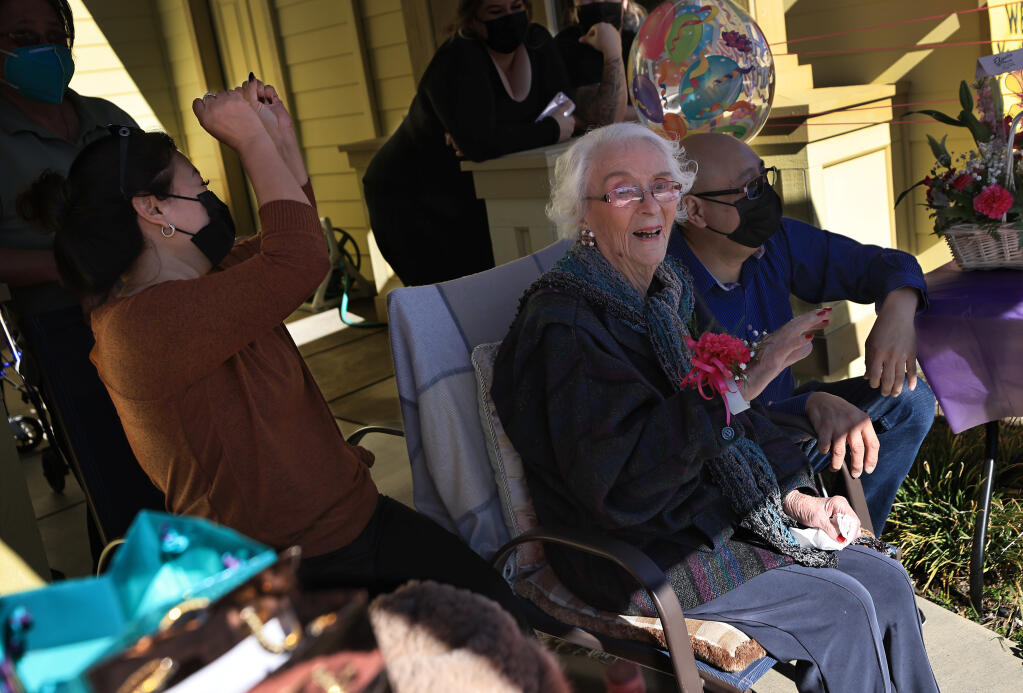 Willits resident Edith “Edie” Ceccarelli, middle, waves to a parade of Willits residents driving by in cars, Saturday, Feb. 5, 2022, to celebrate Ceccarelli turning 114 years old. Perla Gonzalez, left, reacts as Edie acknowledges her friends. Genaro Gonzalez, right and Perla operate Holy Spirit Inc. a residential care facility where Ceccarelli lives. (Kent Porter / The Press Democrat)