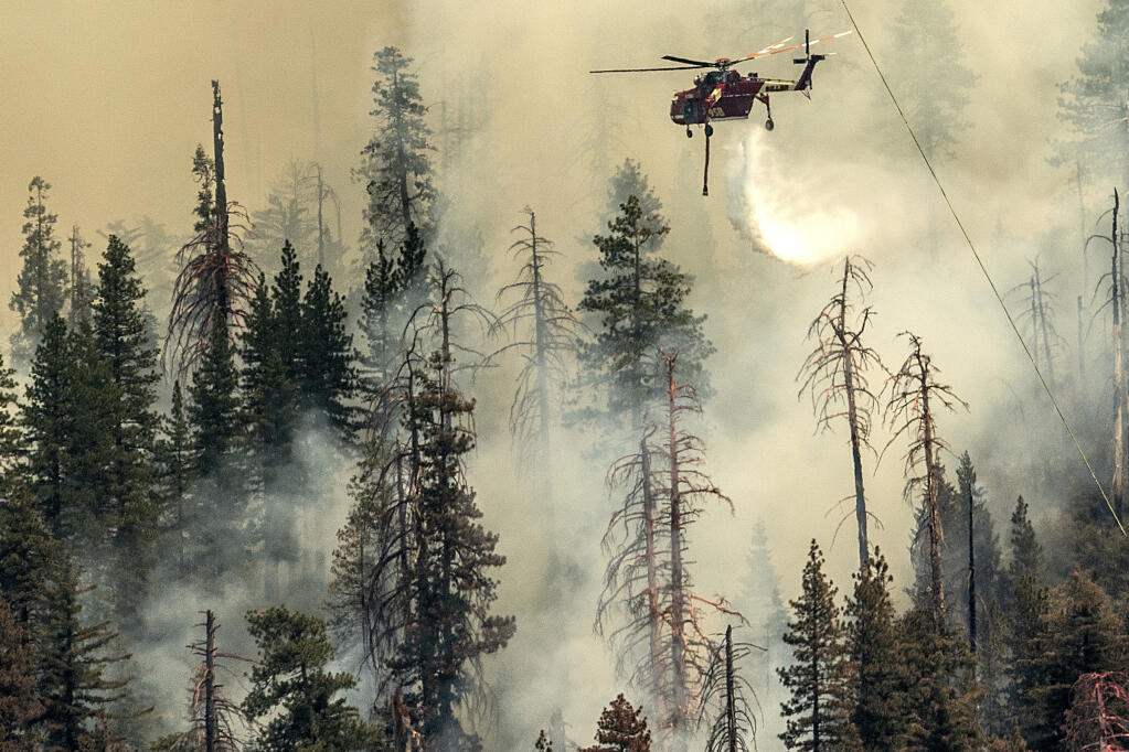 Seen from unincorporated Mariposa County, Calif., a helicopter drops water on the Washburn Fire burning in Yosemite National Park, Saturday, July 9, 2022. (AP Photo/Noah Berger)