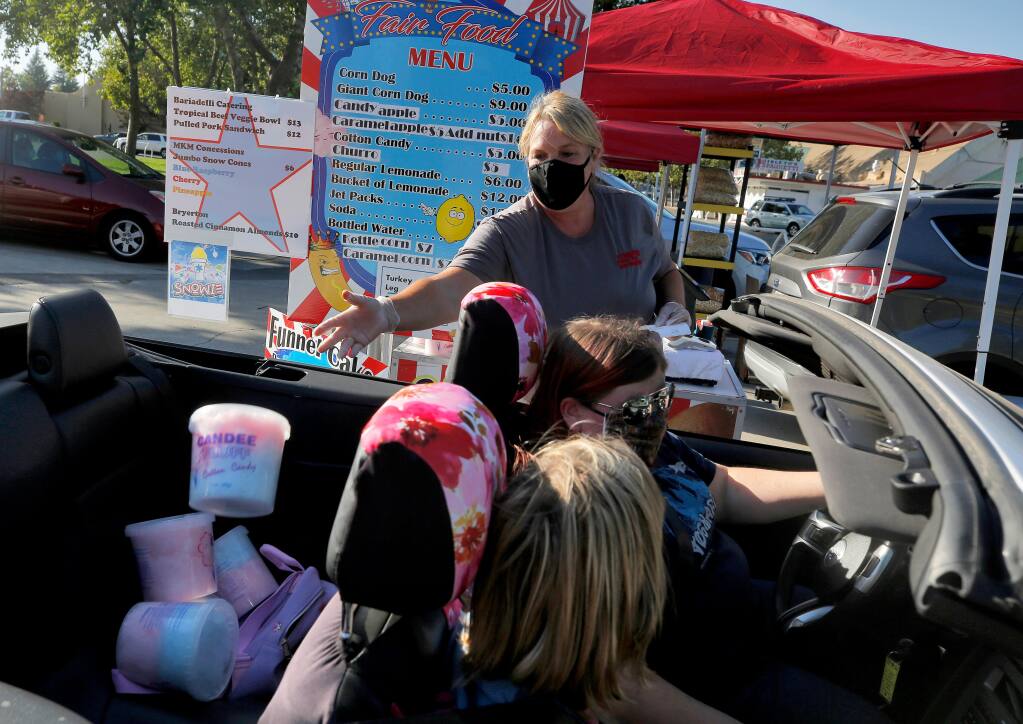 Stacee Hoffee tosses buckets of cotton candy into the back seat of Chelsea Carlson's convertible, as Chelsea and her friend Danielle Bowman pick up their families' fair food orders during the Fair Food Frenzy drive-thru at the Sonoma County Fairgrounds in Santa Rosa, California, on Friday, August 7, 2020. (Alvin A.H. Jornada / The Press Democrat)