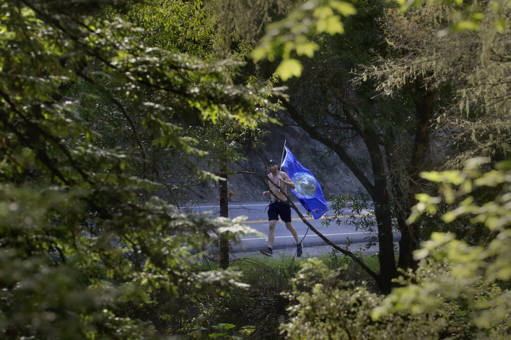 Kyle Gift runs along Bohemian Highway from his home in Camp Meeker to Monte Rio carrying an Earth flag to raise awareness for forest care and management. Photo taken near Monte Rio, Calif., on Thursday, April 7, 2022. (Beth Schlanker/The Press Democrat)