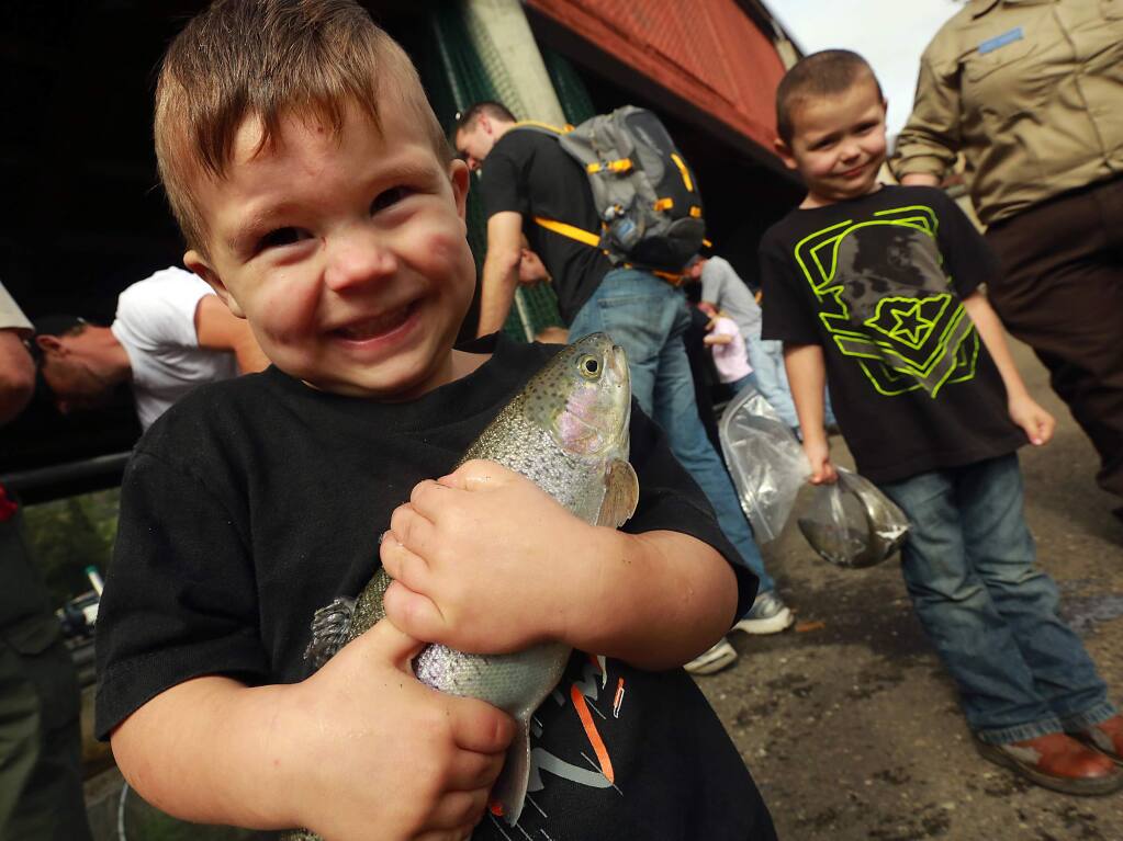 Deegan Mack, 3, of Cloverdale proudly clings to the steelhead fish he caught with his dad and brother Gunner, 5, right, at the Lake Sonoma Steelhead Festival. (Photo by John Burgess/The Press Democrat)