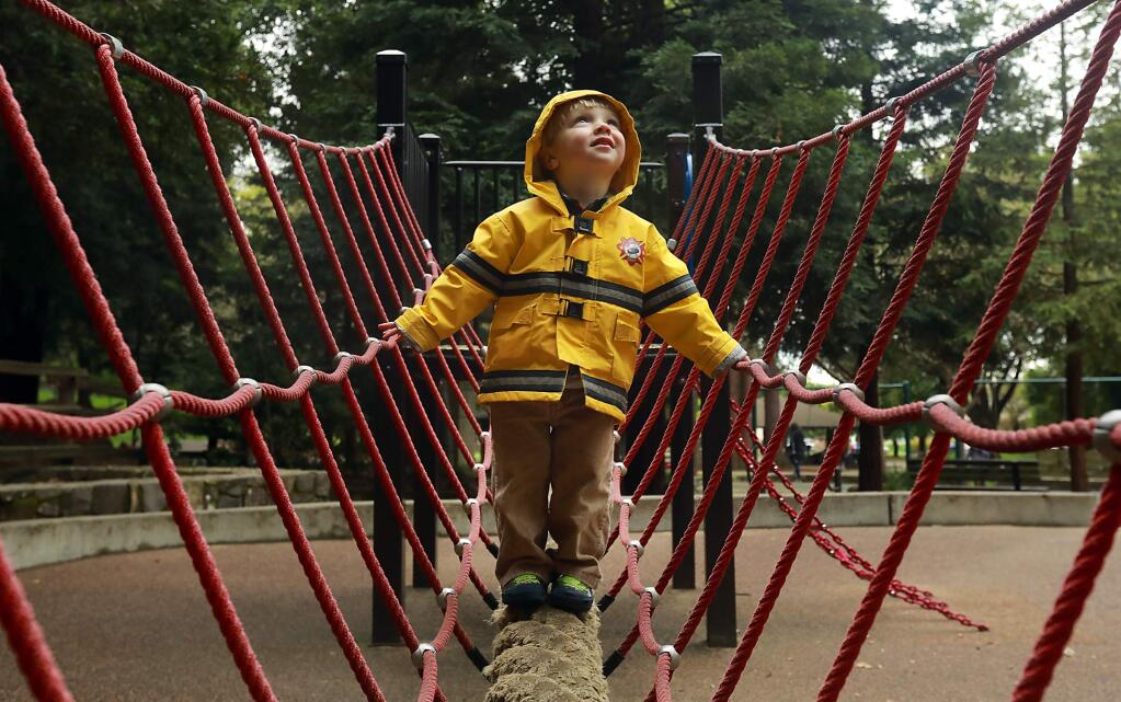 Sidney Sholley, 2, of Santa Rosa was prepared for the rain with his yellow firefighter rain slicker on the rope bridge at Howarth Park on Thursday. (John Burgess/The Press Democrat)
