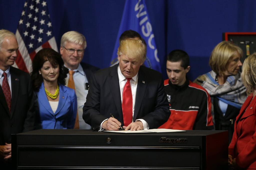 President Donald Trump signs an executive order to tighten the rules for technology companies seeking to bring highly skilled foreign workers to the U.S., Tuesday, April 18, 2017, at Snap-On Tools in Kenosha, Wis. Sen. Ron Johnson, R-Wis. is at left, Rep. Glenn Grothman, R-Wis. is third from left. Education Secretary Betsy DeVos is at right. (AP Photo/Kiichiro Sato)