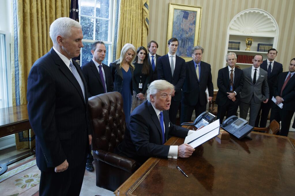 President Donald Trump, accompanied by Vice President Mike Pence, and staff, talks with reporters in the Oval Office of the White House in Washington, Tuesday, Jan. 24, 2017. (AP Photo/Evan Vucci)