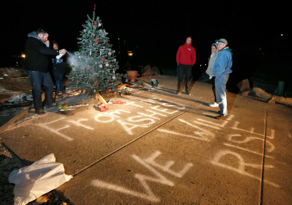 Ronnie Duvall, far left, sprays flocking on a decorated Christmas tree on Rita Place as his friends look on, in the Coffey Park neighborhood of Santa Rosa, California on Monday, December 11, 2017. (Alvin Jornada / The Press Democrat)