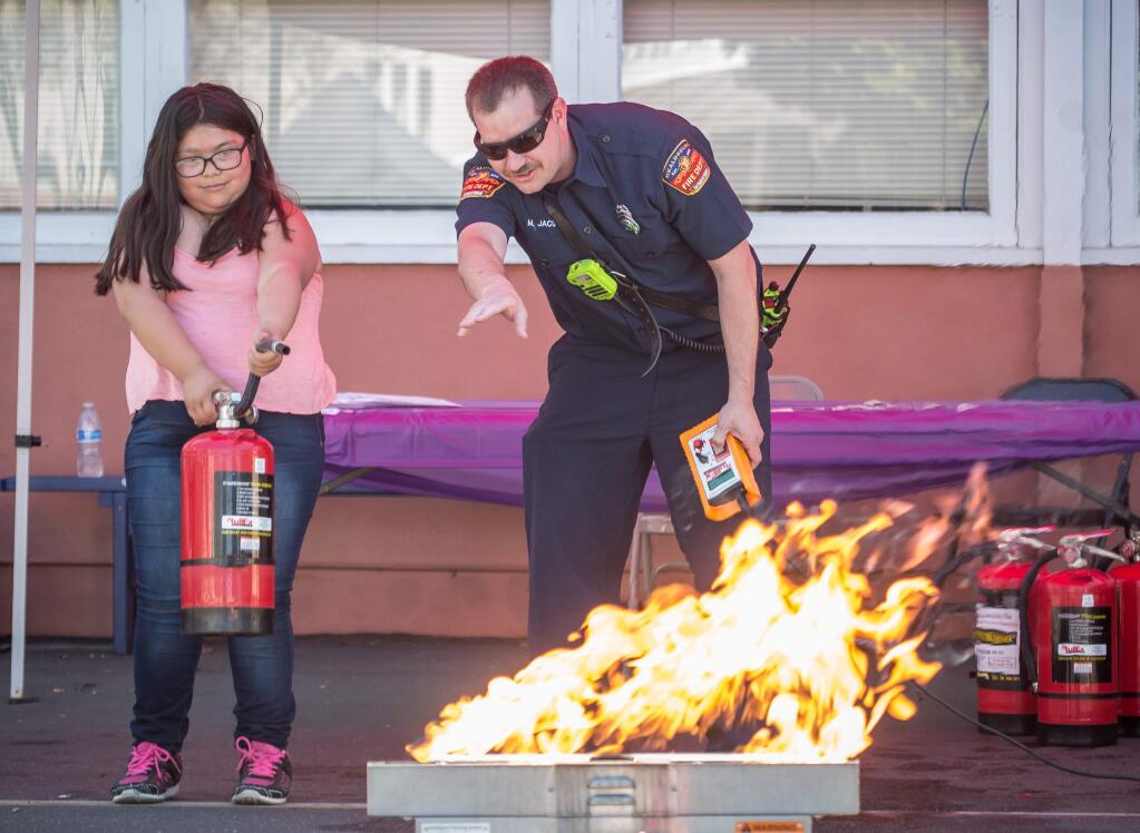 Laylah Gutierrez gets help from Mike Jacobs, of the Healdsburg Fire Department, while learning how to use a fire extinguisher during a “Safe and United Community Event” Sunday April 2, 2017, at the Saint John's Church in Healdsburg, Calif. The Healdsburg Police Department, in conjunction with the Fire Department, Community Services, Corazon Healdsburg, and several other nonprofit organizations hosted the event to inform Latinos of their rights and their support in the community. (Jeremy Portje / For The Press Democrat)