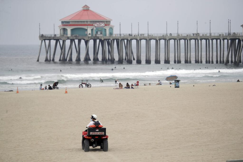 A lifeguard wears a mask while patroling the beach Thursday, April 30, 2020, in Huntington Beach, Calif. California Gov. Gavin Newsom has ordered beaches in Orange County to close until further notice amid the COVID-19 pandemic. Newsom made the announcement Thursday, days after tens of thousands of people in Orange County packed beaches during a sunny weekend. (AP Photo/Marcio Jose Sanchez)