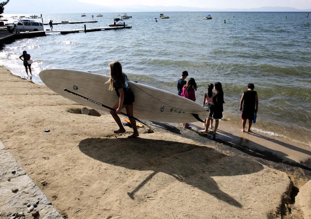 In this photo taken Tuesday, Aug. 8, 2017, Jessica Brackett, of South Tahoe Standup Paddle, carries a paddle board along the shore of Lake Tahoe, in South Lake, Calif. Lake Tahoe's known for summer and winter fun, but there's a third side to Tahoe: fall, when crowds thin out, rates are cheaper, weather's mild and there's even some leaf-peeping. (AP Photo/Rich Pedroncelli)