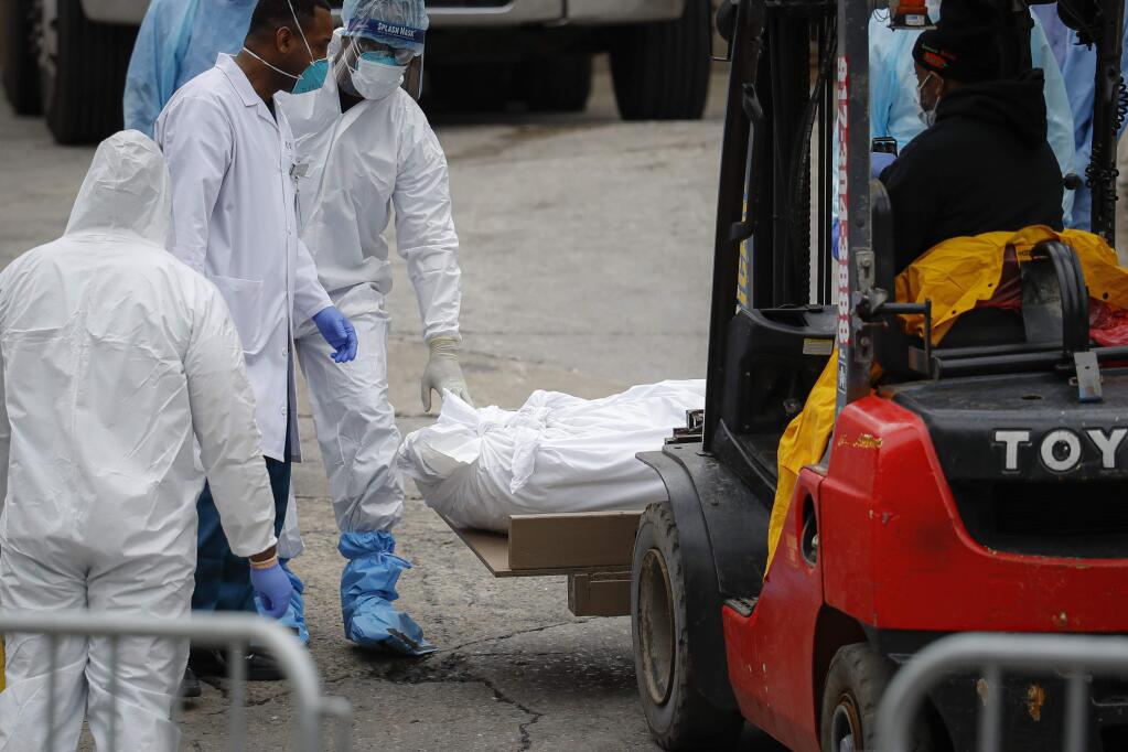 A body wrapped in plastic is prepared to be loaded onto a refrigerated container truck used as a temporary morgue by medical workers due to COVID-19 concerns, Tuesday, March 31, 2020, at Brooklyn Hospital Center in the Brooklyn borough of New York. The new coronavirus causes mild or moderate symptoms for most people, but for some, especially older adults and people with existing health problems, it can cause more severe illness or death. (AP Photo/John Minchillo)