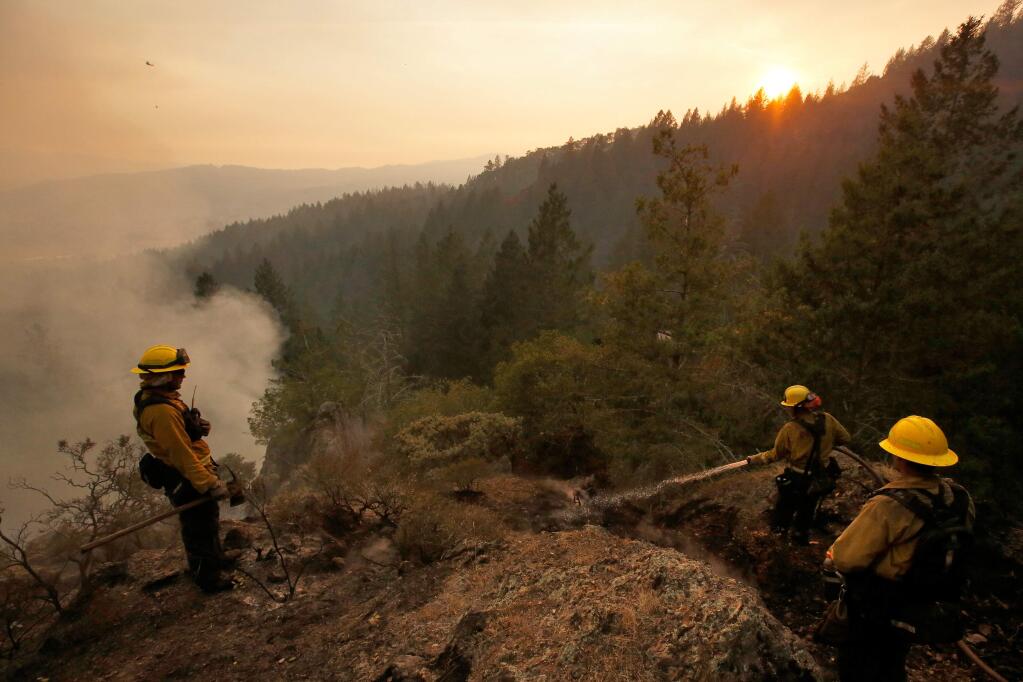 Firefighters Julien Lecorps, left, Clyde Rust and John Farrell of Strike Team 4235A from the Tahoe basin, extinguish hot spots in rugged terrain above homes near Hood Mountain Regional Park while the Nuns Fire continues to burn near Santa Rosa, California on Monday, October 16, 2017. (Alvin Jornada / The Press Democrat)