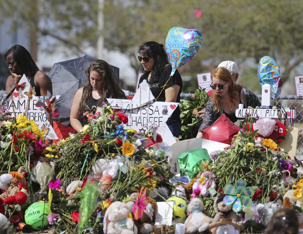 FILE - In this Feb. 25, 2018 file photo, mourners bring flowers as they pay tribute at a memorial for the victims of the shooting at Marjory Stoneman Douglas High School, in Parkland, Fla. The community of Parkland, Florida, is focusing on suicide prevention programs after two survivors of the Florida high school massacre there killed themselves this month. Parkland Mayor Christine Hunschofsky said Monday, March 25, 2019, that officials are publicizing the available counseling services after a second Marjory Stoneman Douglas High School student apparently killed himself over the weekend. (David Santiago/Miami Herald via AP, File)