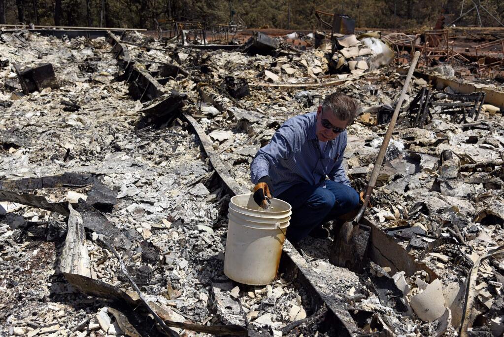 Wayne Fischer sifts through the ashes of his home after it was destroyed by the Rocky Fire near Lower Lake on Sunday, August 2, 2015. Fischer drops coins into a bucket that his wife would collect to give to their grandchildren. (Alvin Jornada for The Press Democrat)